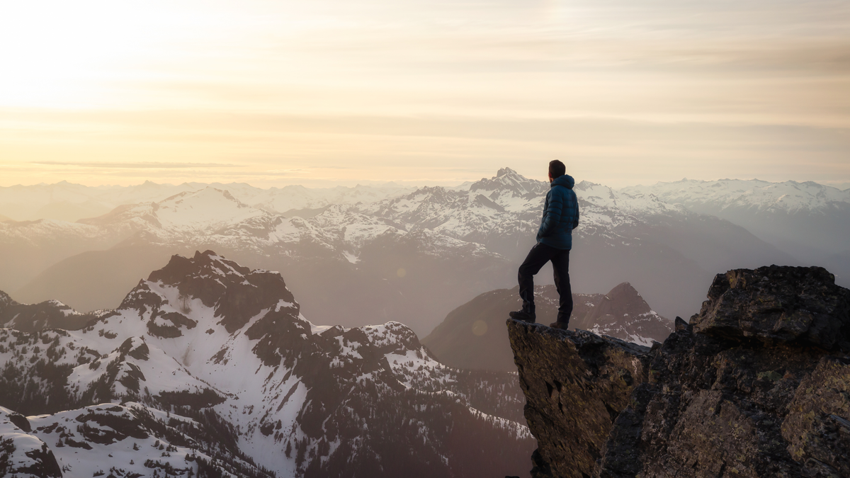 Person standing on a mountain peak with a vast mountain range in the background