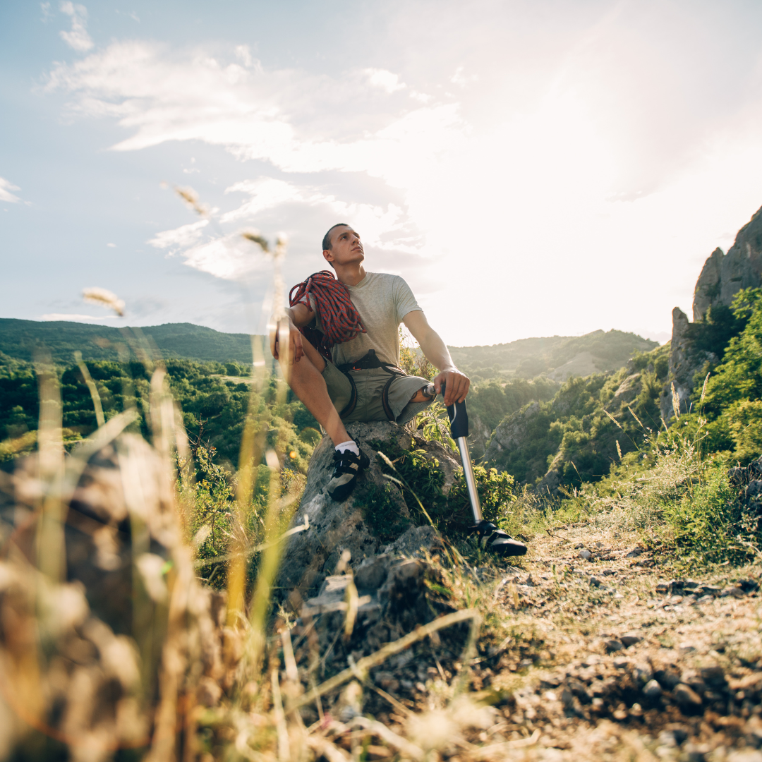 Man sitting on a rock with hiking gear, surrounded by mountains and greenery