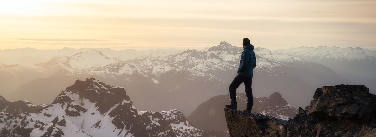 Person standing on a mountain peak with snow-capped mountains in the background